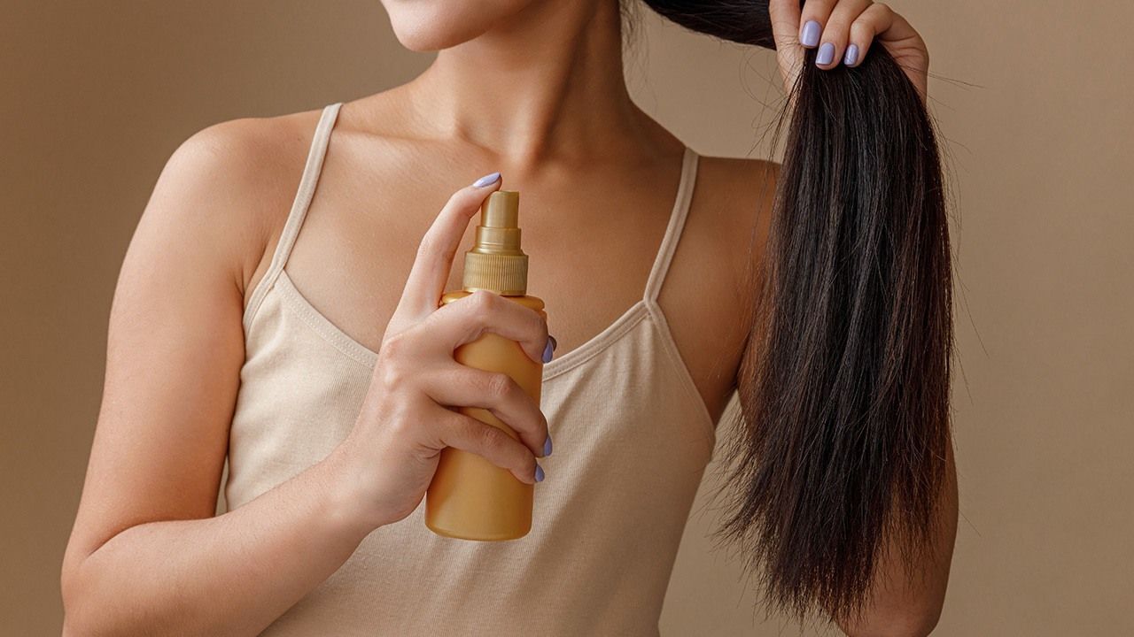 wanita sedang menggunakan spray ke rambut