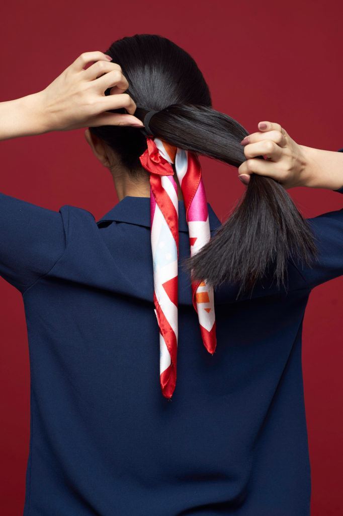 Wanita asia sedang mengikat rambut dengan gaya ponytail – cara menata scarf rambut.