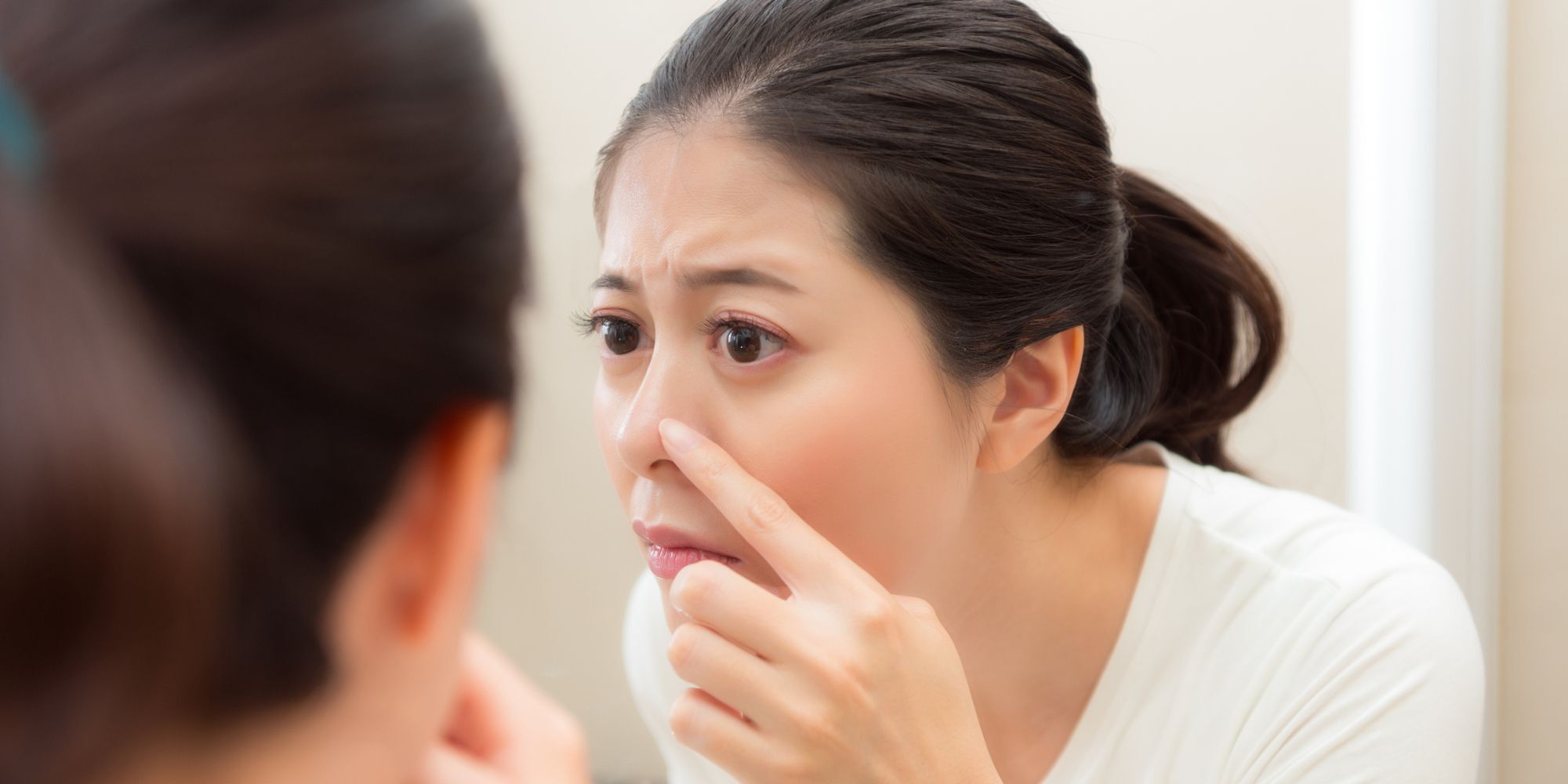wanita berkaca di cermin sambil menyentuh hidung