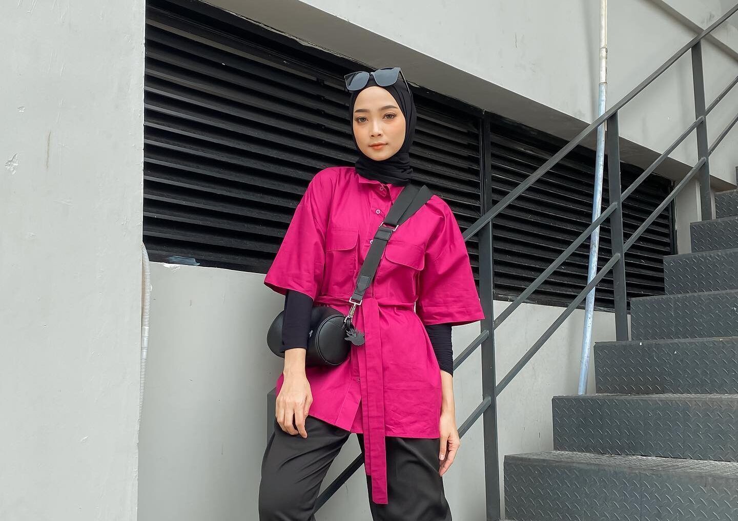 Wanita Indonesia mengenakan padanan baju pink fuchsia dengan hijab warna hitam.
