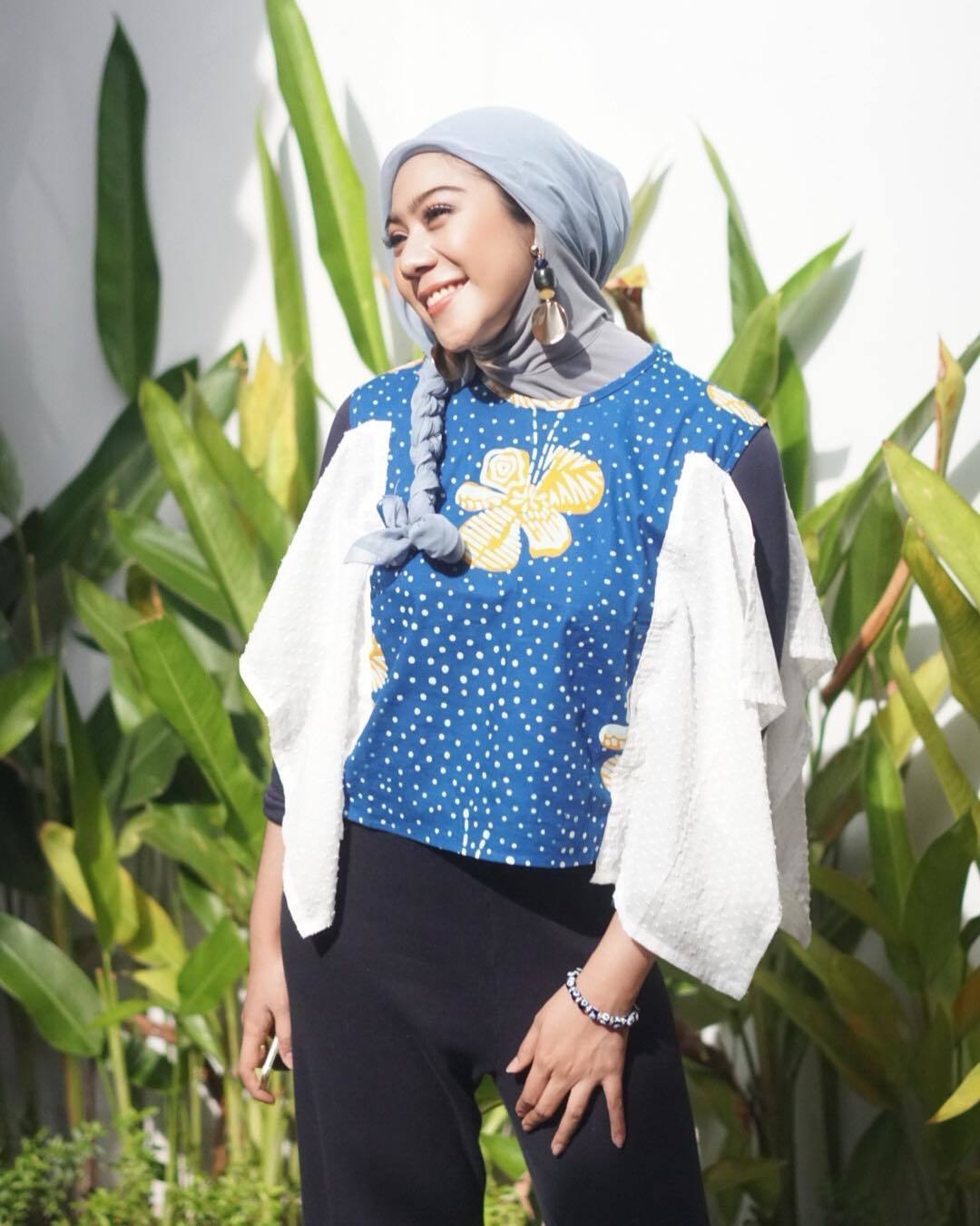 Tiwu Rayi berdiri tesenyum memakai baju dan hijab biru.