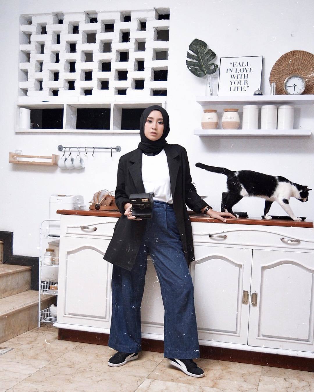 Wanita Asia memakai hijab, blazer, dan wide leg jeans di dapur.
