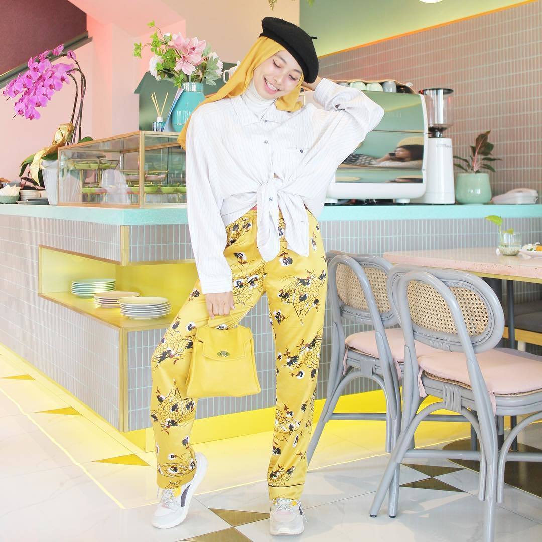 Wanita berhijab memakai celana kuning dan kemeja putih bergaya di kafe.