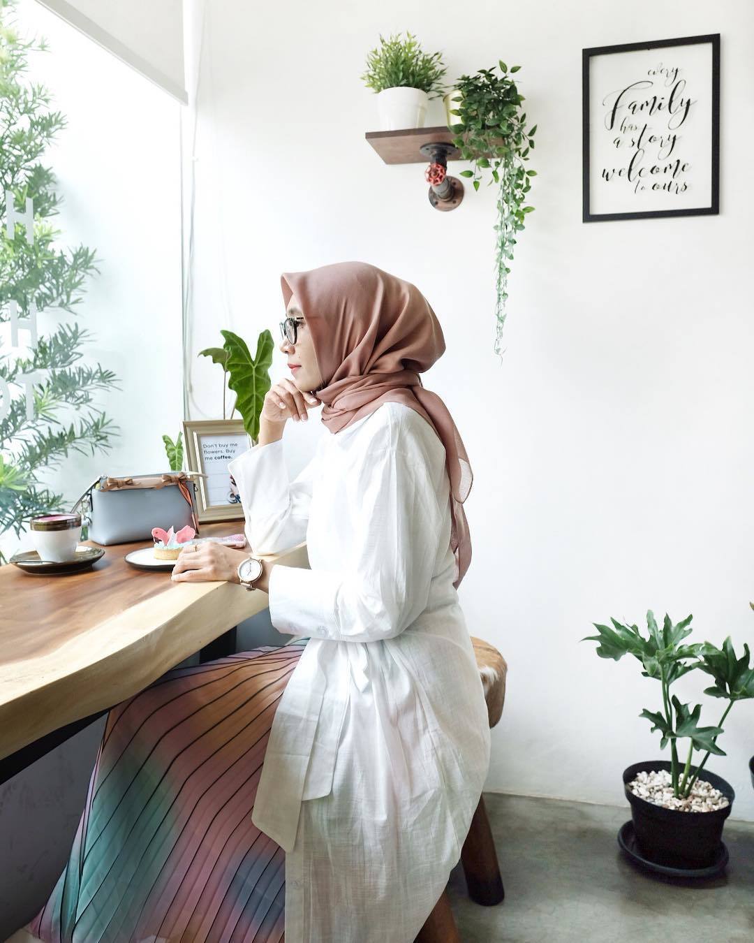 Wanita berhijab duduk di kafe memandang ke luar.