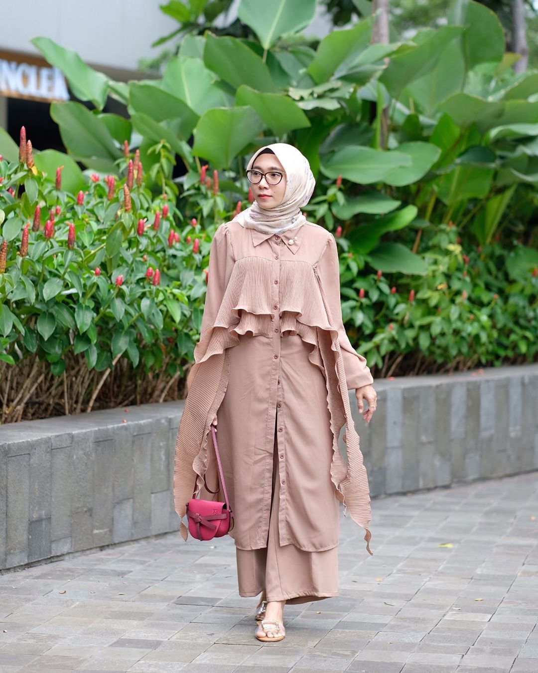 Wanita berhijab dan memakai busana dengan detail flowy berjalan di pinggir jalan.