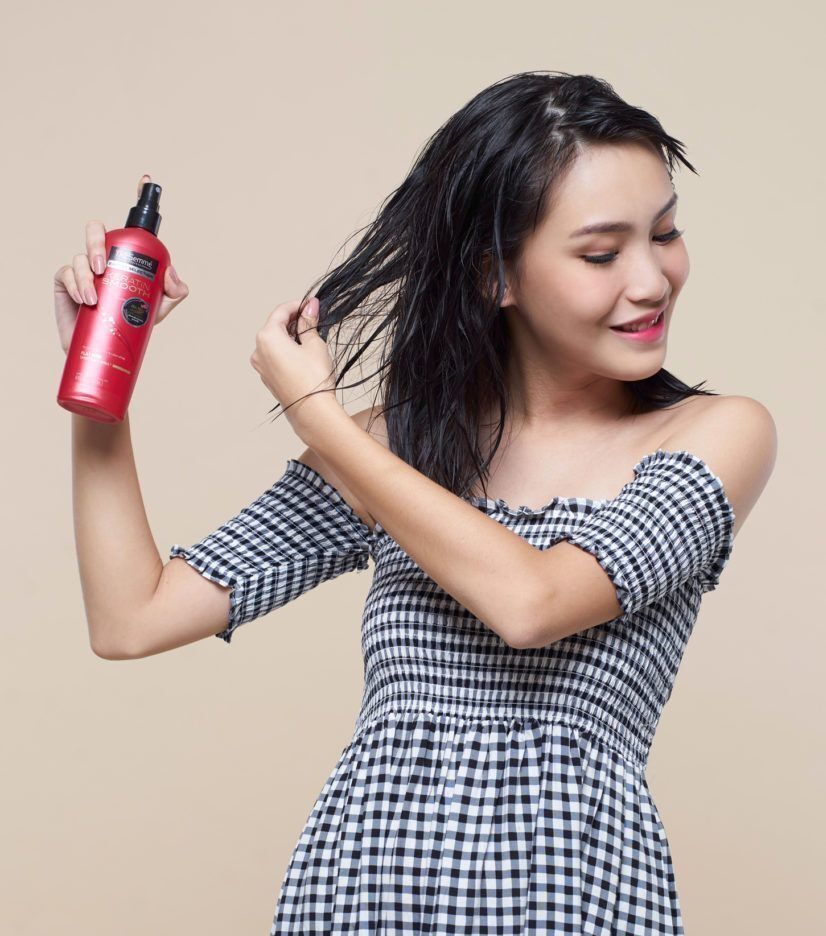 ผู้หญิงเอเชีย ผมประบ่าสีดำ กำลังฉีดสเปรย์กันความร้อนให้ผม