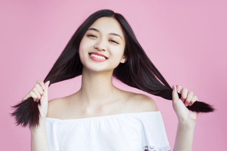 ผู้หญิงเอเชีย ผมดำยาว กำลังจับปลายผมทั้งสองข้างอย่างอารมณ์ดี