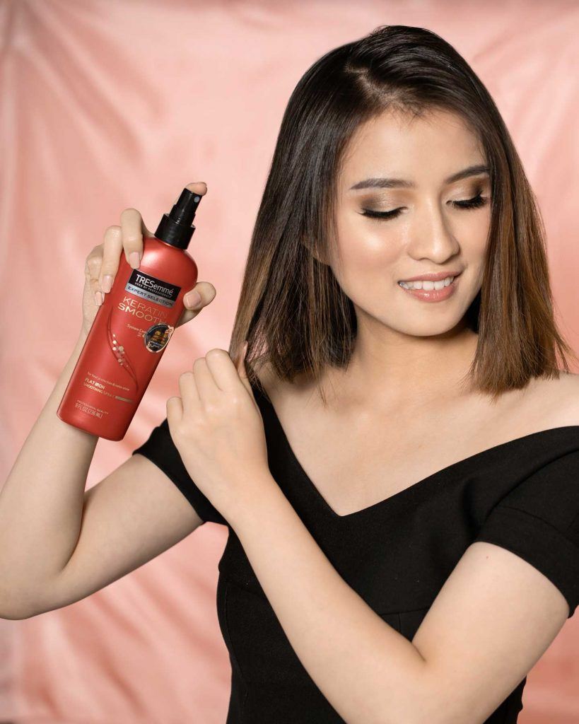 ผู้หญิงเอเชียผมสั้นสีน้ำตาลเข้ม กำลังฉีดสเปรย์กันความร้อนลงบนผม