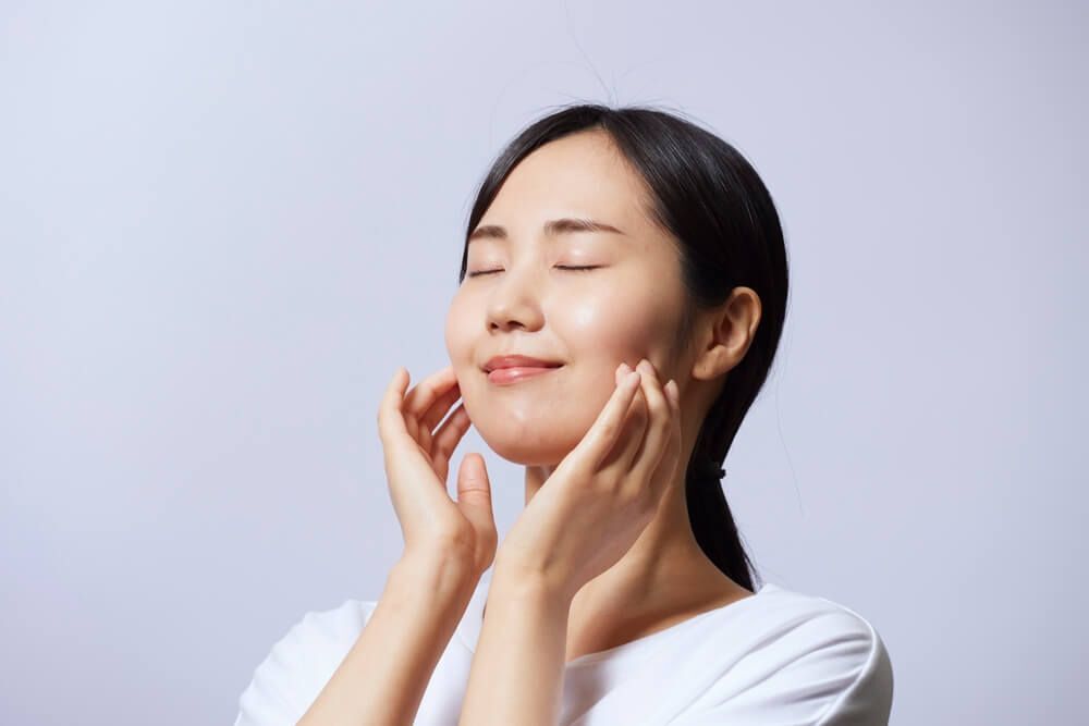 ผู้หญิงเอเชียไว้ผมยาว กำลังจับผิวหน้าตัวเอง เพื่อเช็คผิว