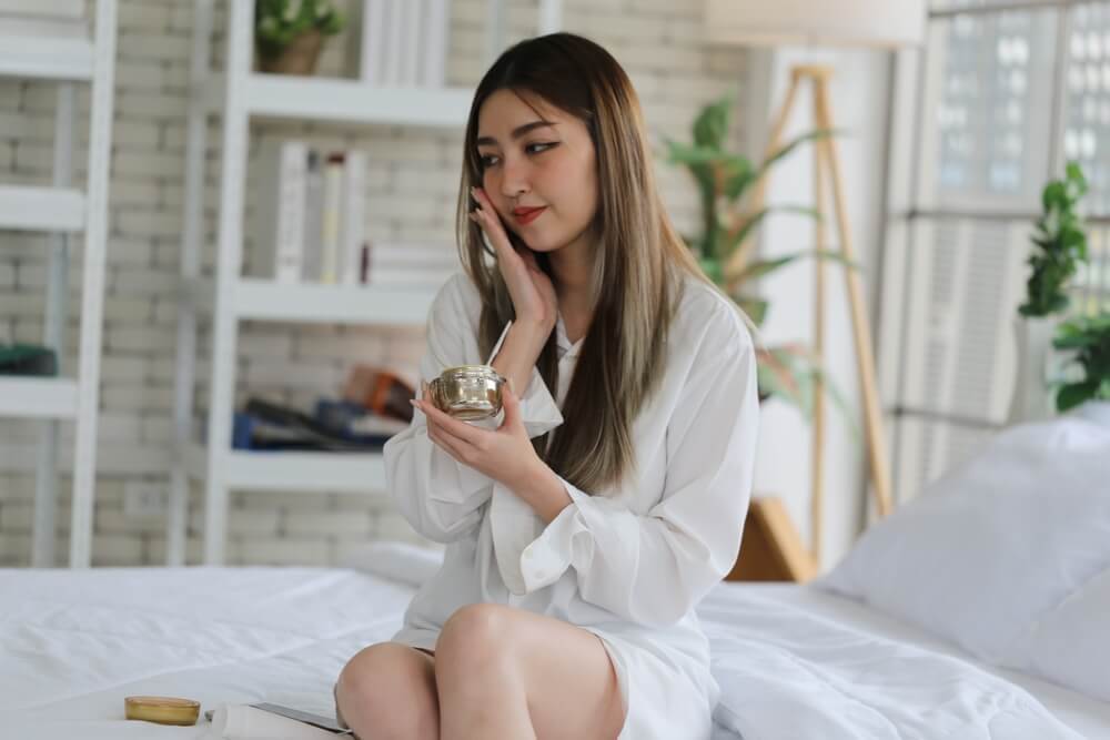 ผู้หญิงเอเชีย ไว้ผมยาว กำลังทาครีมบำรุงผิวหน้า ก่อนเข้านอน