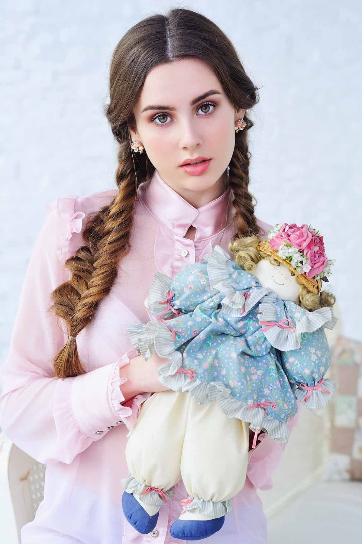 Trendy young girl with two braids hairstyle posing with vintage doll