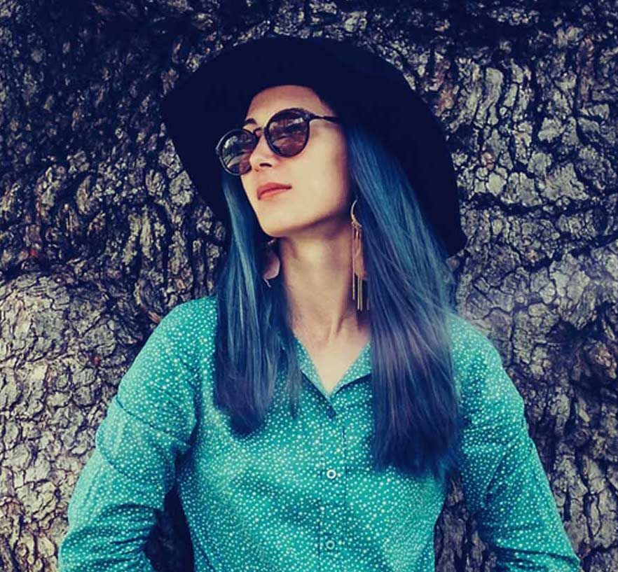 Beautiful fashionable young woman standing near the oak tree in summer park