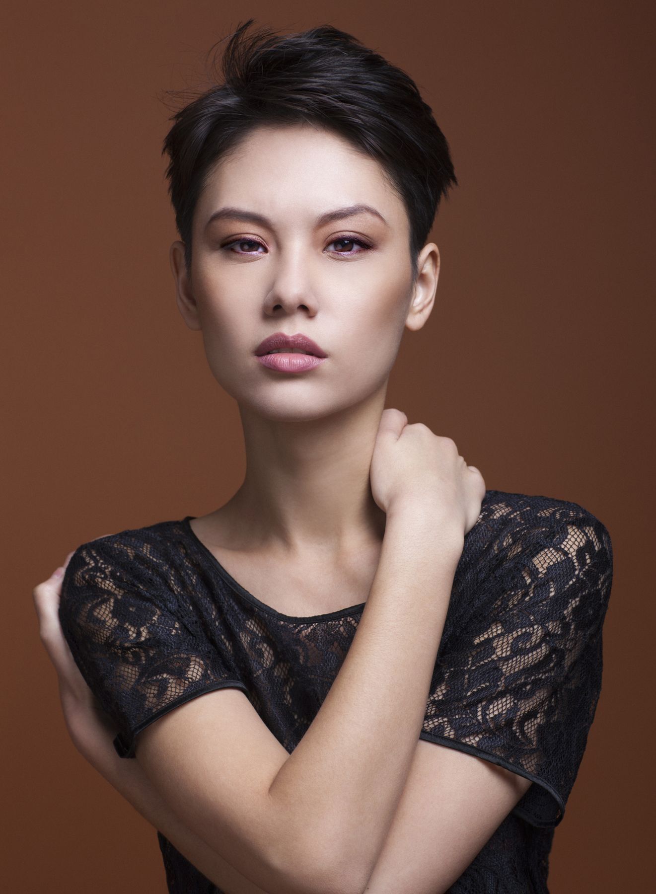 Portrait of a beautiful Asian female model with short black hair wearing a black lace shirt, looking at the camera with her arms crossed.