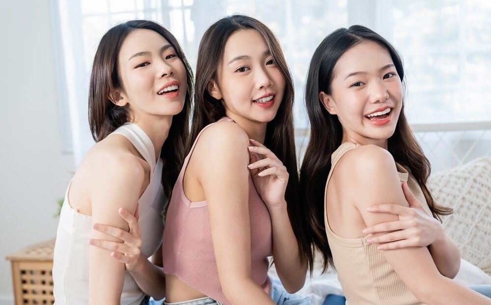 หญิงสาวเอเชีย ผมยาว สามคน เอียงข้าง อวดผิวต้นแขน เลือกครีมบำรุงผิว