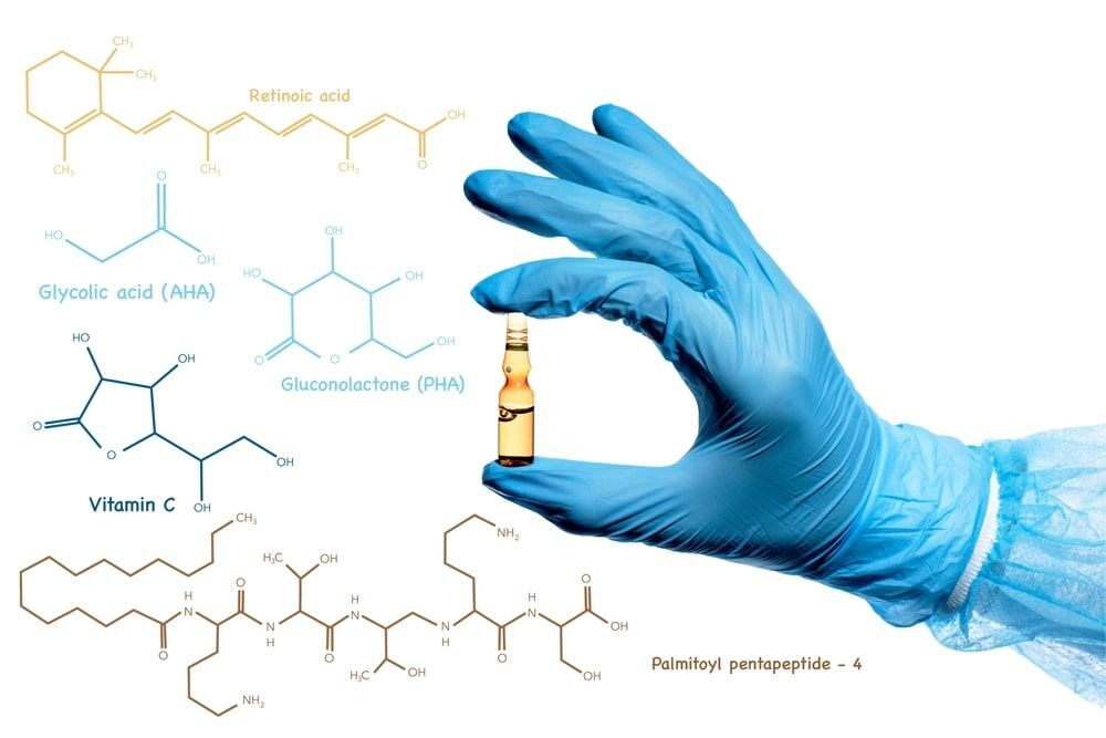 มือใส่ถุงมือสีฟ้าถือขวดแก้วขนาดเล็กบนพื้นหลังกราฟิกเตมีส่วนผสมของเรตินอลในสกินแคร์