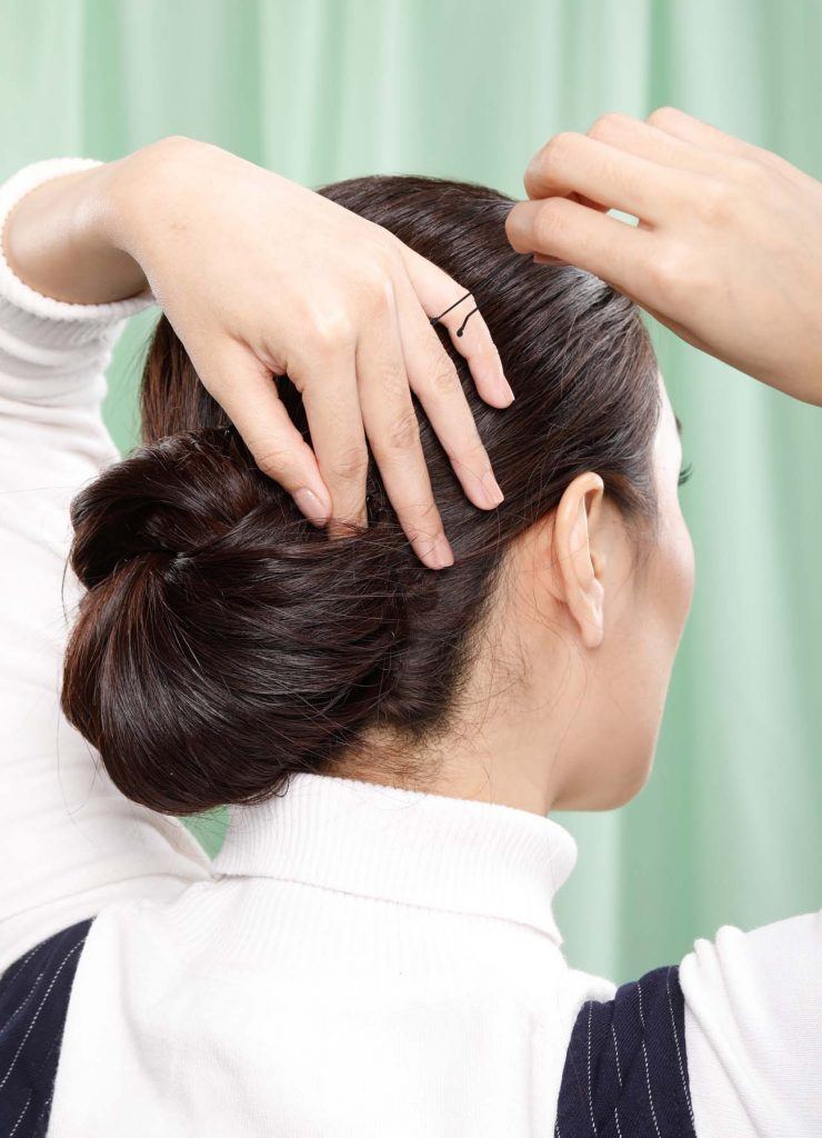 ผู้หญิงเอเชียผมยาวสีดำ กำลังเกล้าผมและติดกิ๊บ