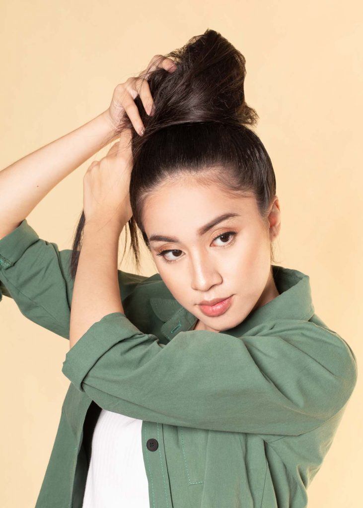 ผู้หญิงเอเชียผมยาว ใส่เสื้อเชิ้ตสีเขียว สาธิตวิธีทำผมทรงดังโงะ