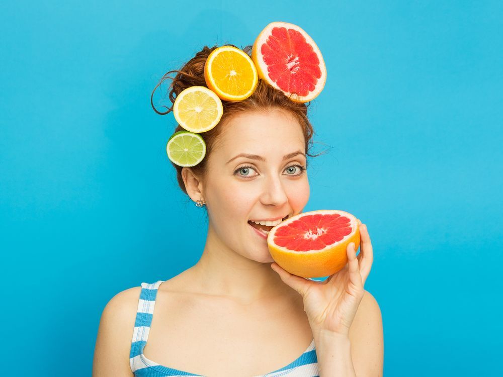 หญิงสาว ผิวขาว แต่งผม ด้วย ผลไม้ตระกูลส้ม ทำท่ากัดเกรปฟรุต ผ่าซีก