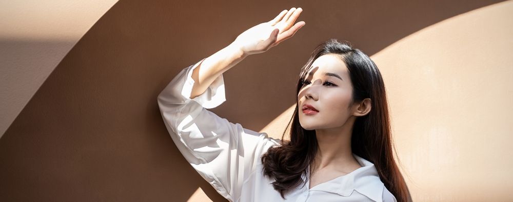 ผู้หญิเอเชียไว้ผมยาว กำลังยกมือข้างหนึ่งขึ้นบังแดด