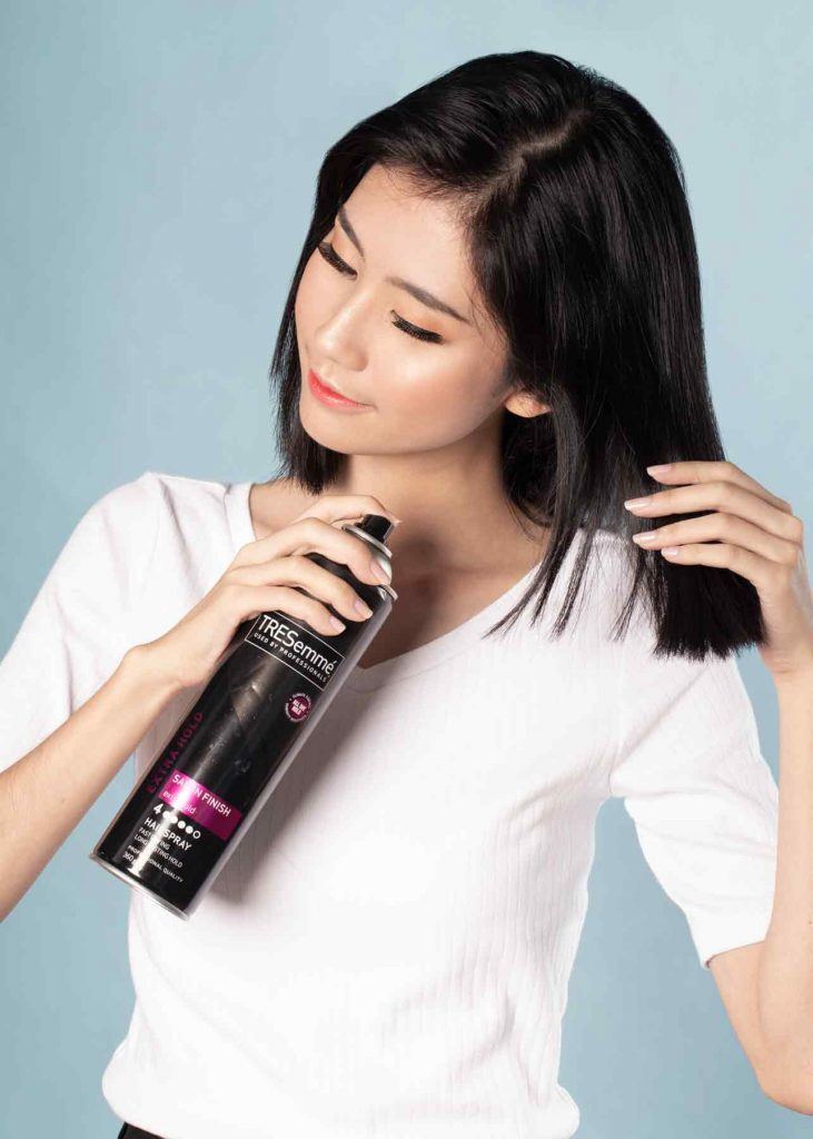 ผู้หญิงเอเชียผมสั้น ใส่เสื้อยืดสีขาว ฉีดสเปรย์แต่งผม