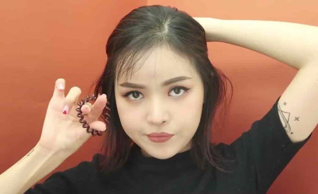 อินฟลูเอนเซอร์ไทย mynjimye ไว้ผมสั้นประบ่าสีดำ กำลังสาธิตการใช้ยางรัดผมมัดผม