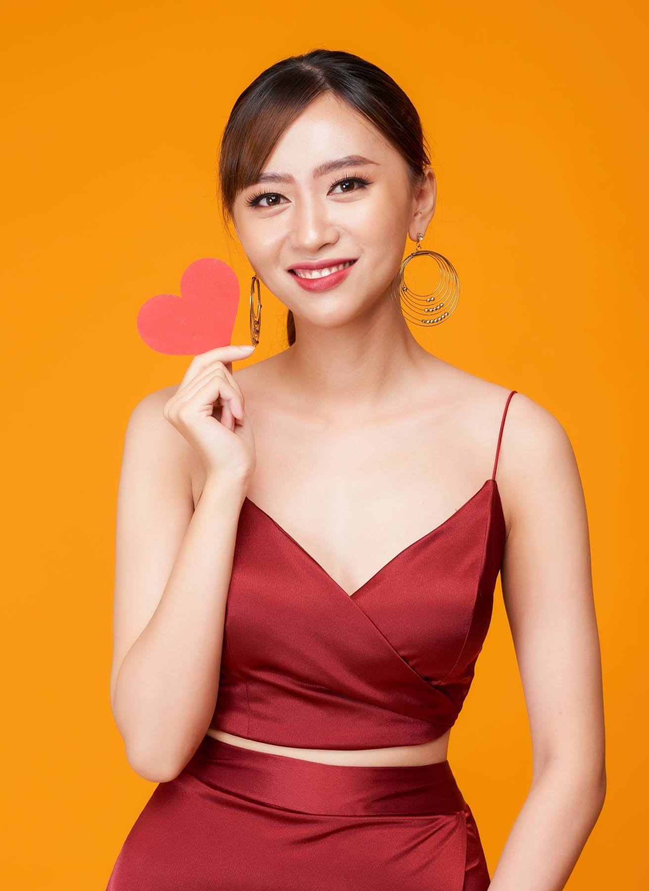 ผู้หญิงเอเชียผมยาวใส่ชุดสายเดี่ยวสีแดง ถือกระดาษรูปหัวใจ วันวาเลนไทน์