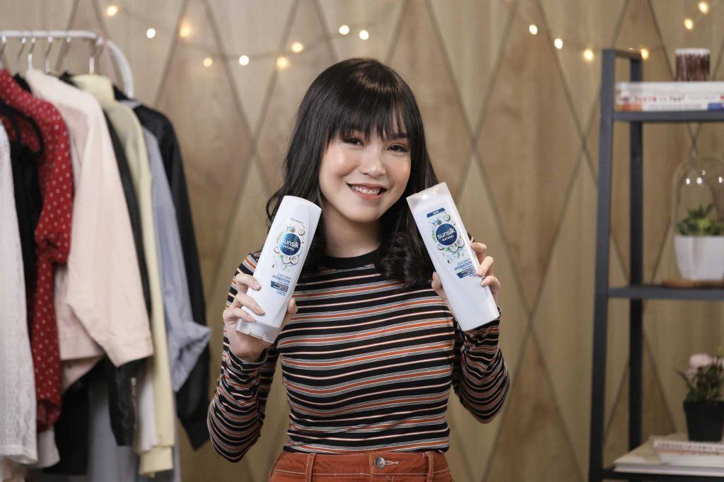 ผู้หญิงเอเชียผมประบ่าสีดำ กำลังถือขวดแชมพูและครีมนวดผม