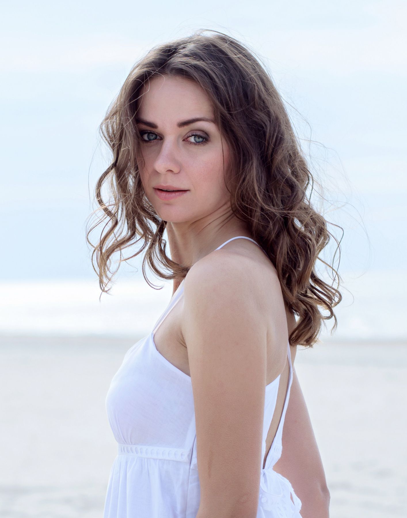ผู้หญิงฝรั่ง ใส่เดรสสายเดี่ยวสีขาว ผมลอนบีชเวฟ ยืนริมทะเล