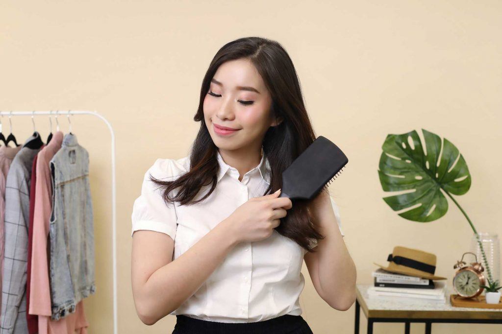 ผู้หญิงเอเชียผมยาวสีดำ กำลังหวีผมด้วยแปรงพาย