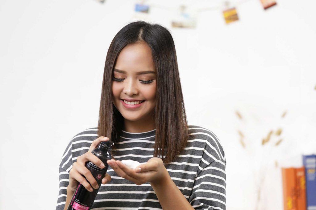 ผู้หญิงเอเชียผมยาวประบ่าสีดำ กำลังบีบมูสลงบนฝ่ามือ