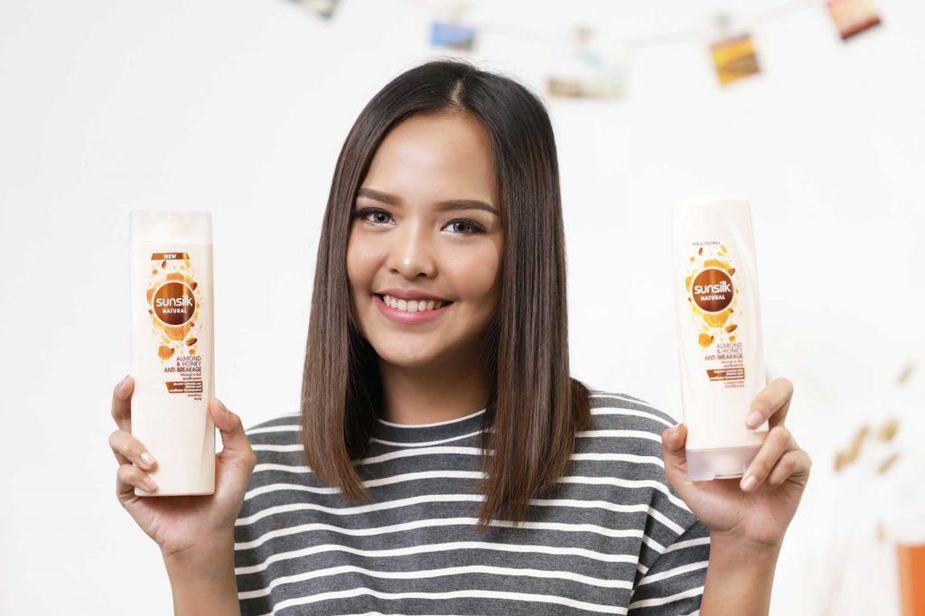 ผู้หญิงเอเชียผมยาวประบ่าสีดำ กำลังถือขวดแชมพูและครีมนวดผม