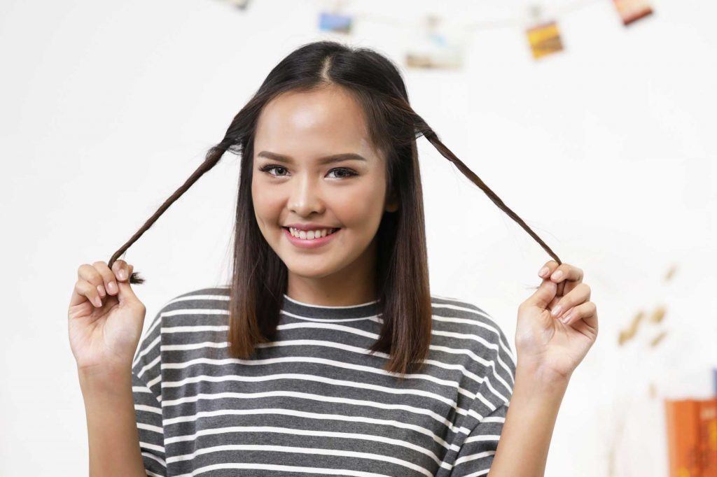 ผู้หญิงเอเชียผมยาวประบ่าสีดำ กำลังบิดผมให้เป็นเกลียว