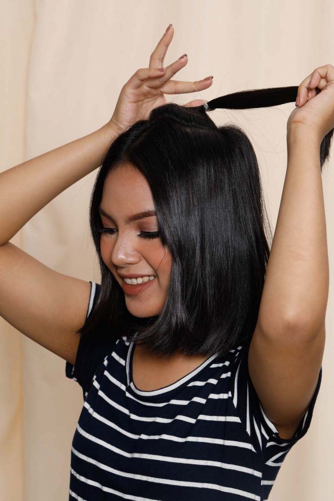 ผู้หญิงเอเชียหน้ากลมผิวคล้ำผมสั้น กำลังมัดผม