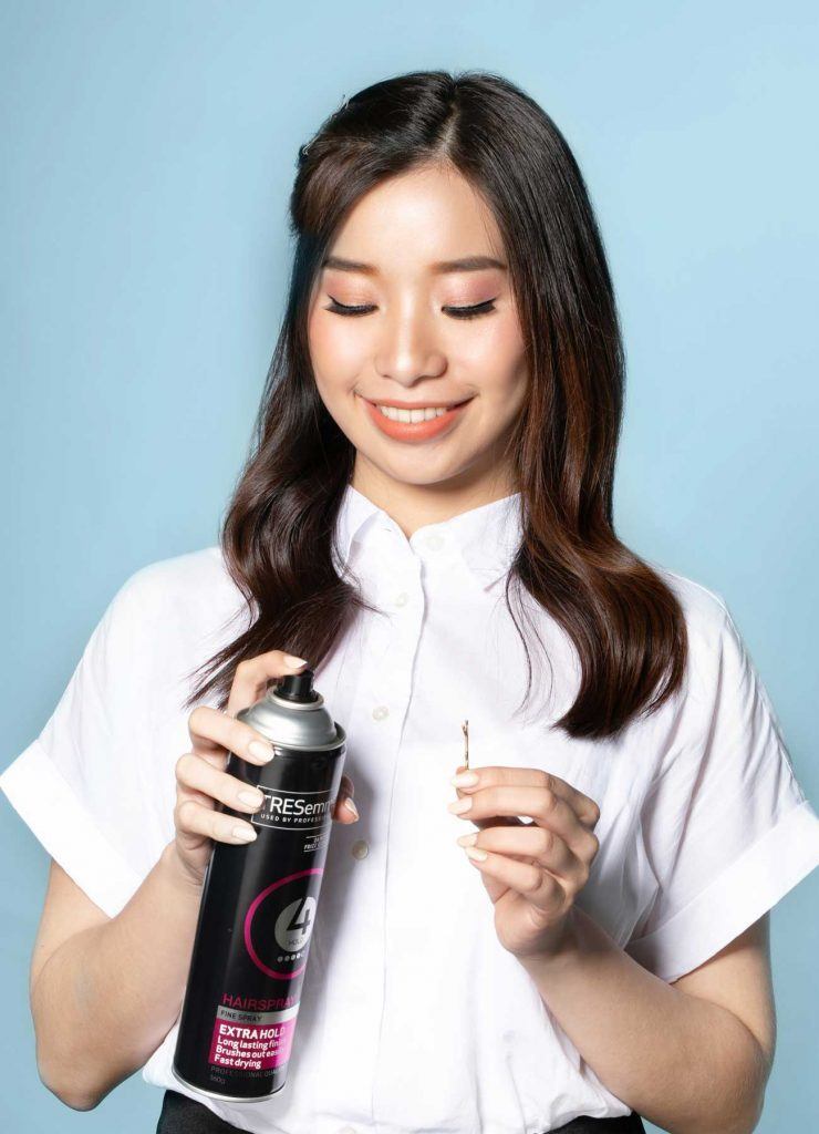 ผู้หญิงเอเชียผมยาว กำลังฉีดสเปรย์แต่งผมลงบนกิ๊บดำ