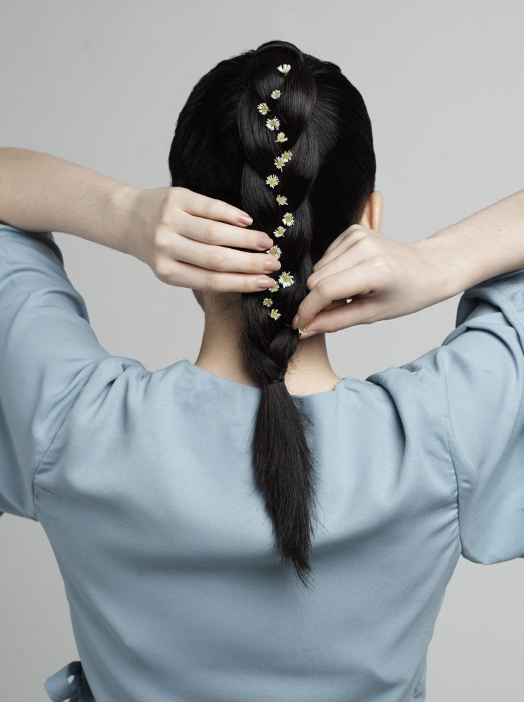 ผู้หญิงผมยาวสีดำ ถักเปียหางม้า สวมเสื้อสีฟ้า ติดดอกไม้