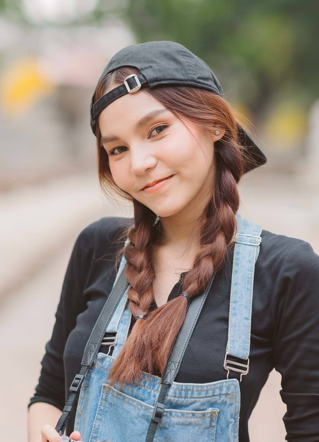 ผู้หญิงเอเชียผมยาวสีน้ำตาล ถักเปียสองข้าง ใส่หมวกแก๊ป