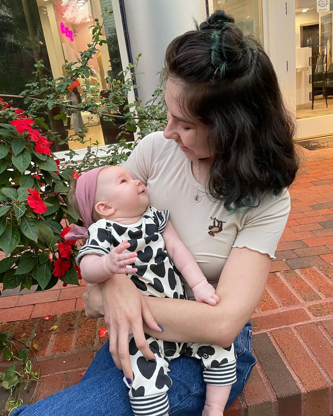 ผู้หญิงฝรั่งผมสีน้ำตาลเข้ม ไว้ผมยาวประบ่ามัดผมจุกครึ่งหัวกำลังอุ้มลูก ทรงผมแม่ลูกอ่อน