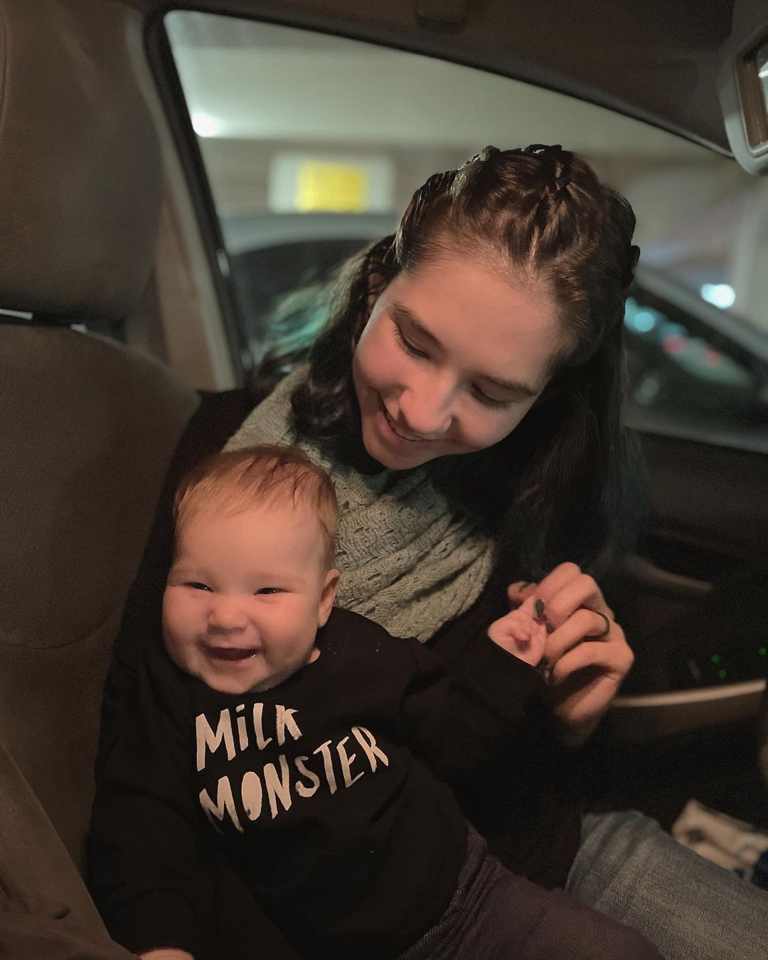 ผู้หญิงฝรั่งผมสีน้ำตาลเข้ม ไว้ผมยาวประบ่ามัดผมจุกครึ่งหัวกำลังอุ้มลูก ทรงผมแม่ลูกอ่อน