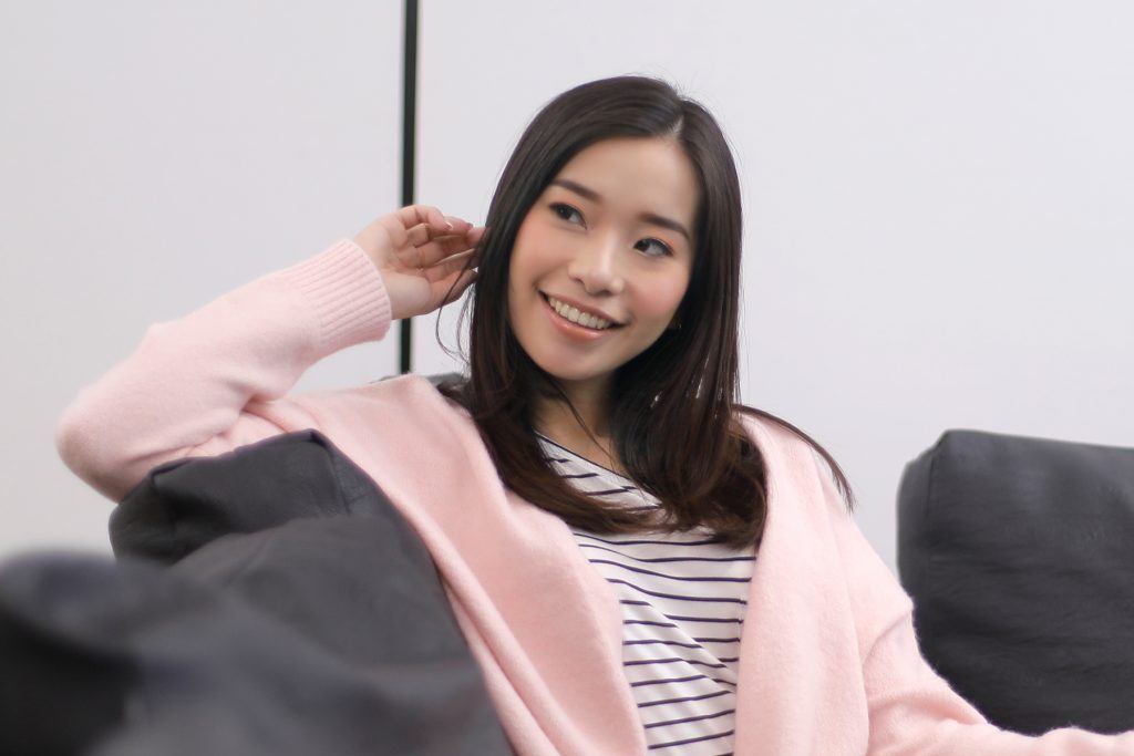 ผู้หญิงเอเชียผมยาวสีดำ กำลังนั่งบนโซฟา มือข้างหนึ่งจับผม