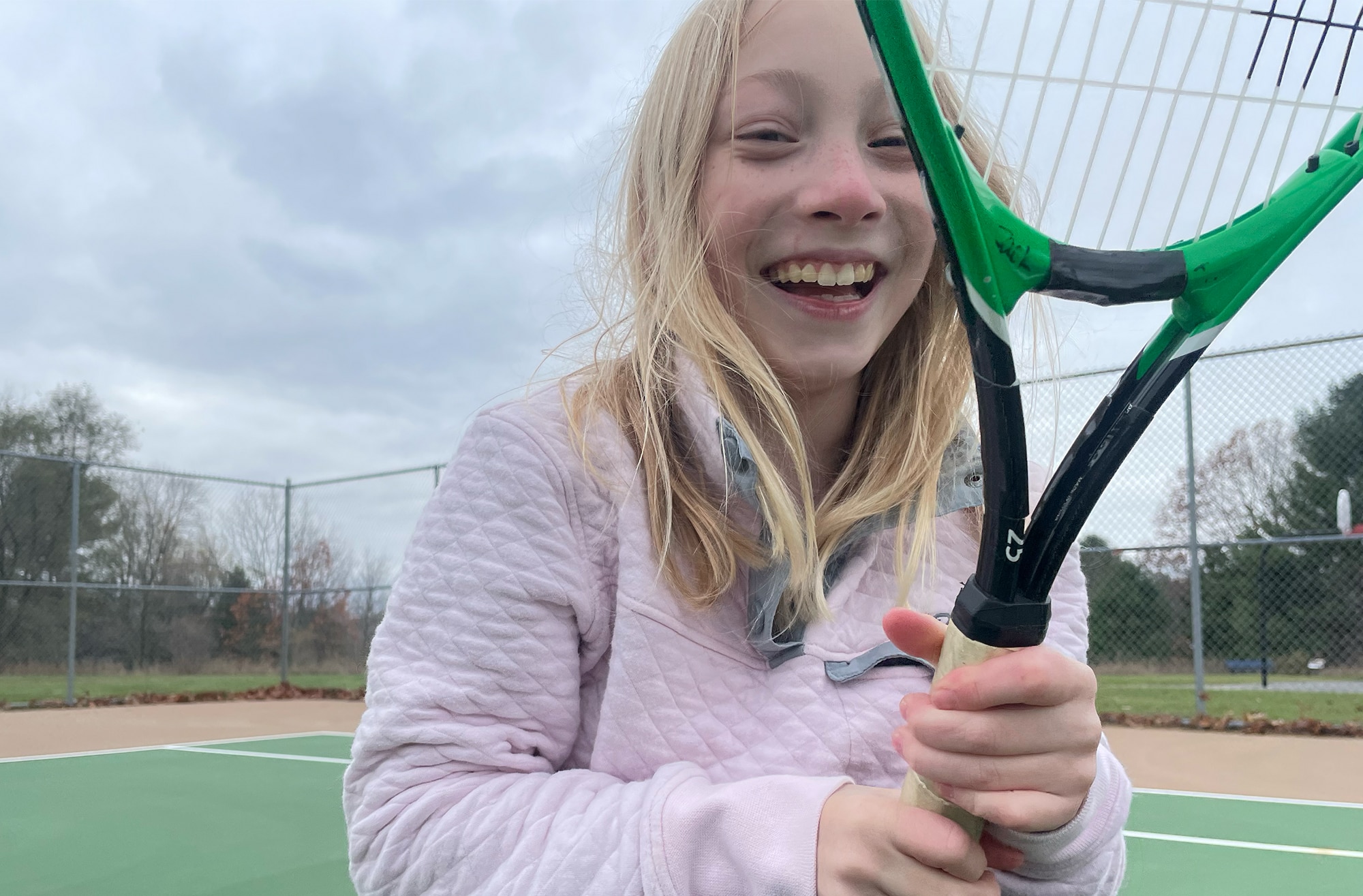 Maya smiling holding a tennis racket on a tennis court