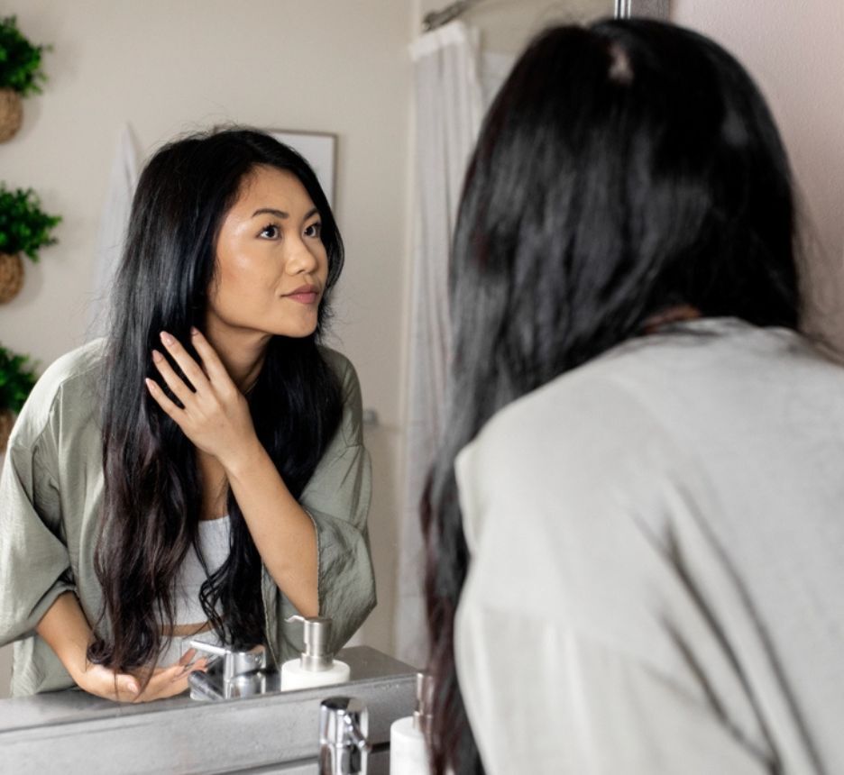 Woman looking at her long hair in front of the mirror.