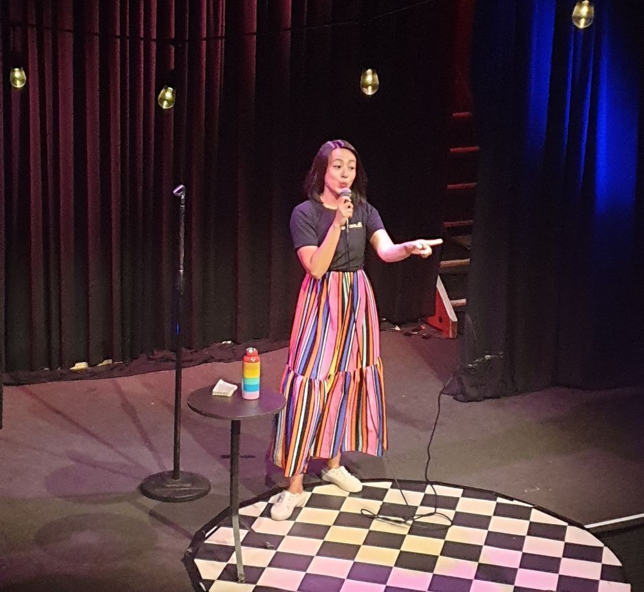 Female comic in colorful skirt doing standup show. 