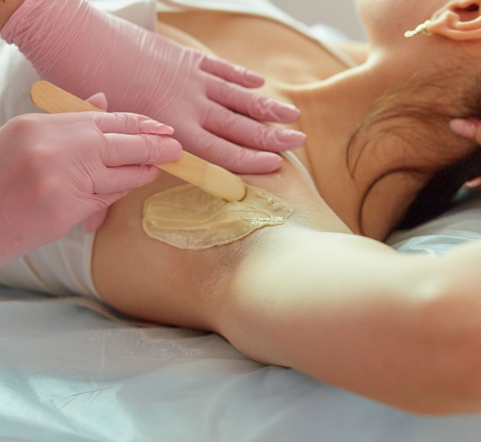 Closeup of waxer‘s hands applying wax on client’s underarm.