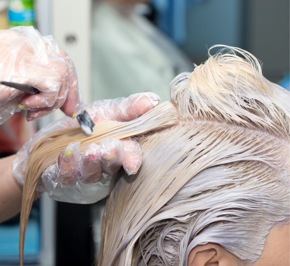 A hair colorist bleaching her client’s long hair.