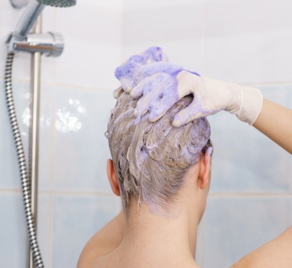 Woman washing her hair with purple shampoo in the shower.