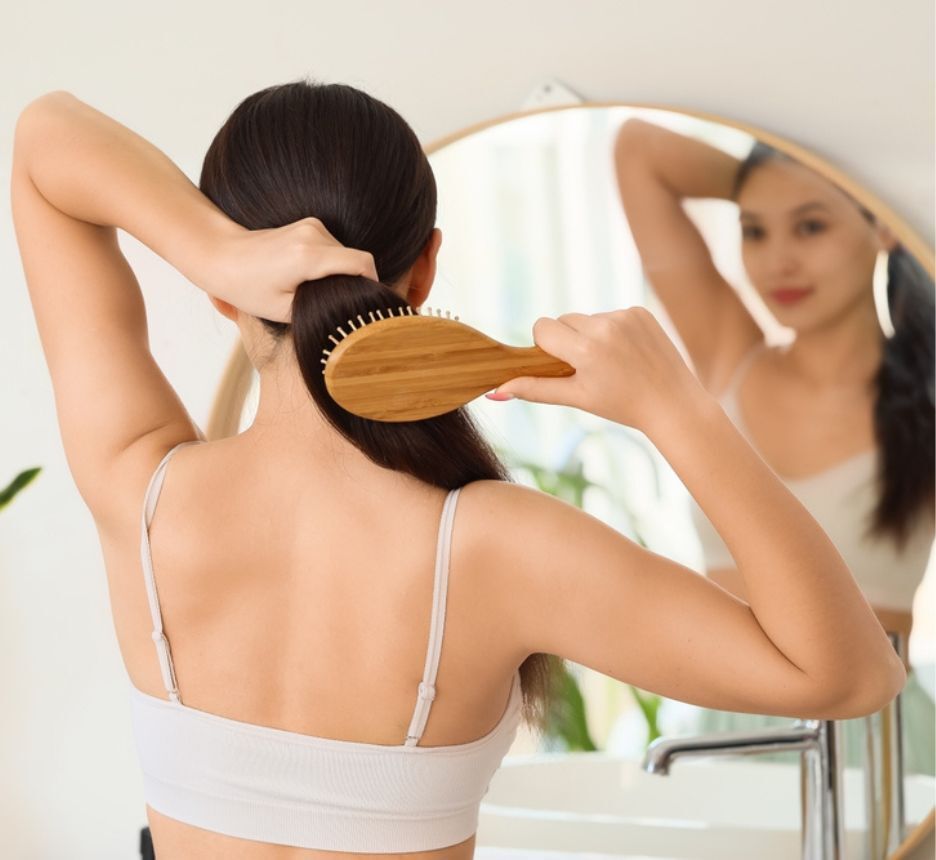 Woman brushing her long hair in front of a mirror.