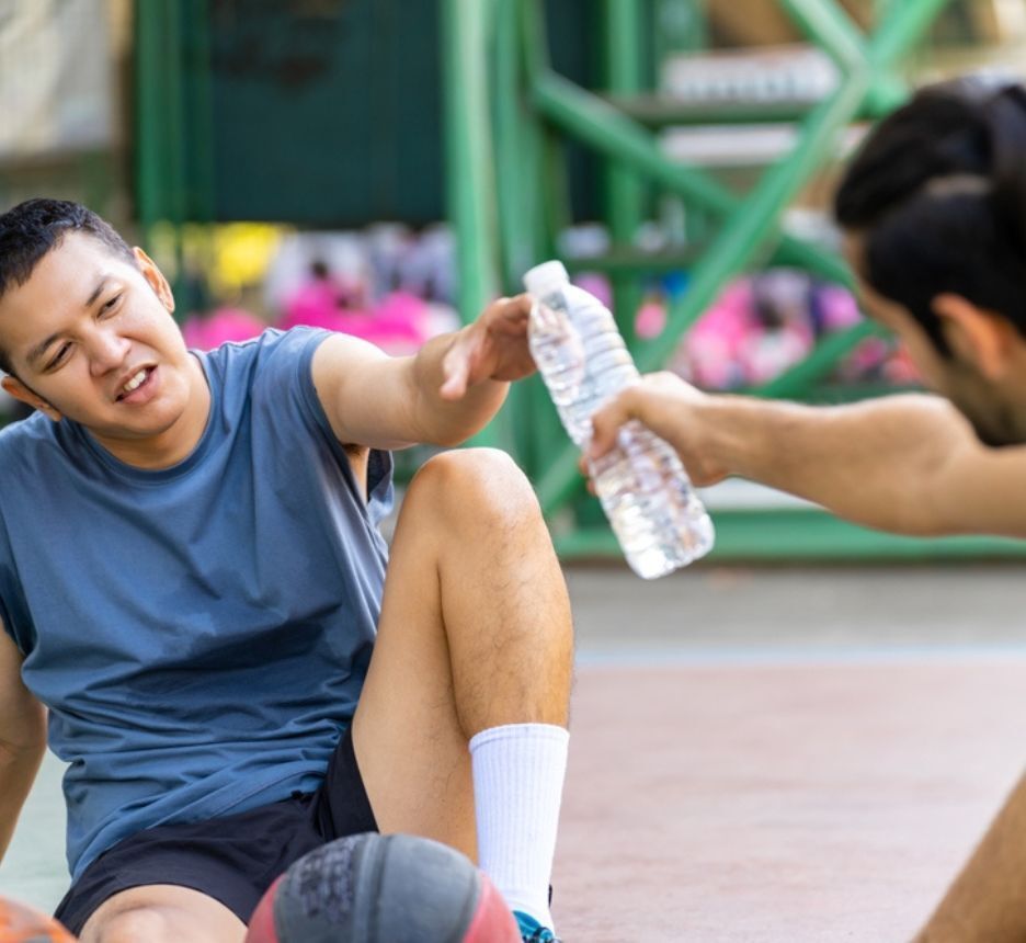 Two men resting and drinking water after a basketball match.