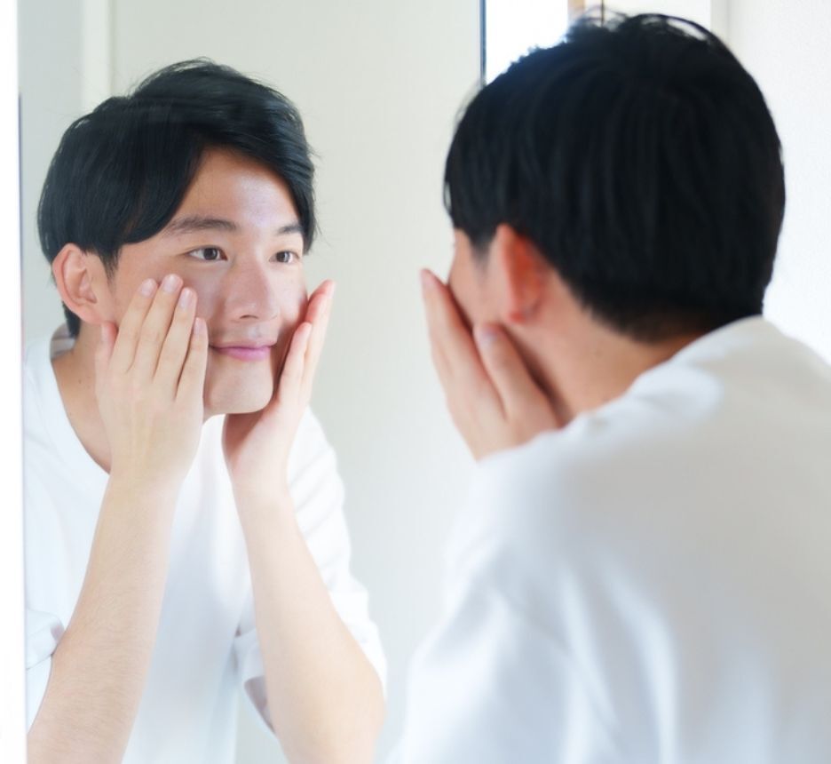 young asian man taking care of his skin looking at reflection in mirror