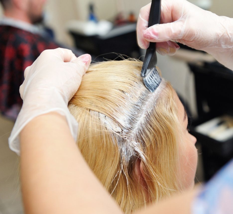 A hair colorist touching up her client’s hair roots with bleach.