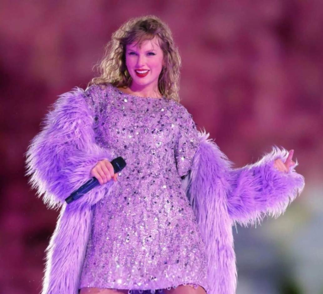 Taylor Swift singing at her concert while wearing purple fur coat.